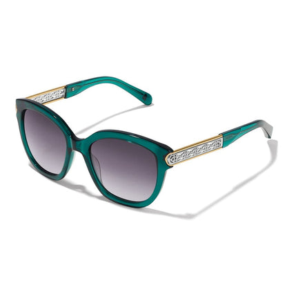 Front view of Green-framed Intrigue Emerald Sunglasses with black gradient lenses stand on a white surface; a metallic emblem decorates the temples.