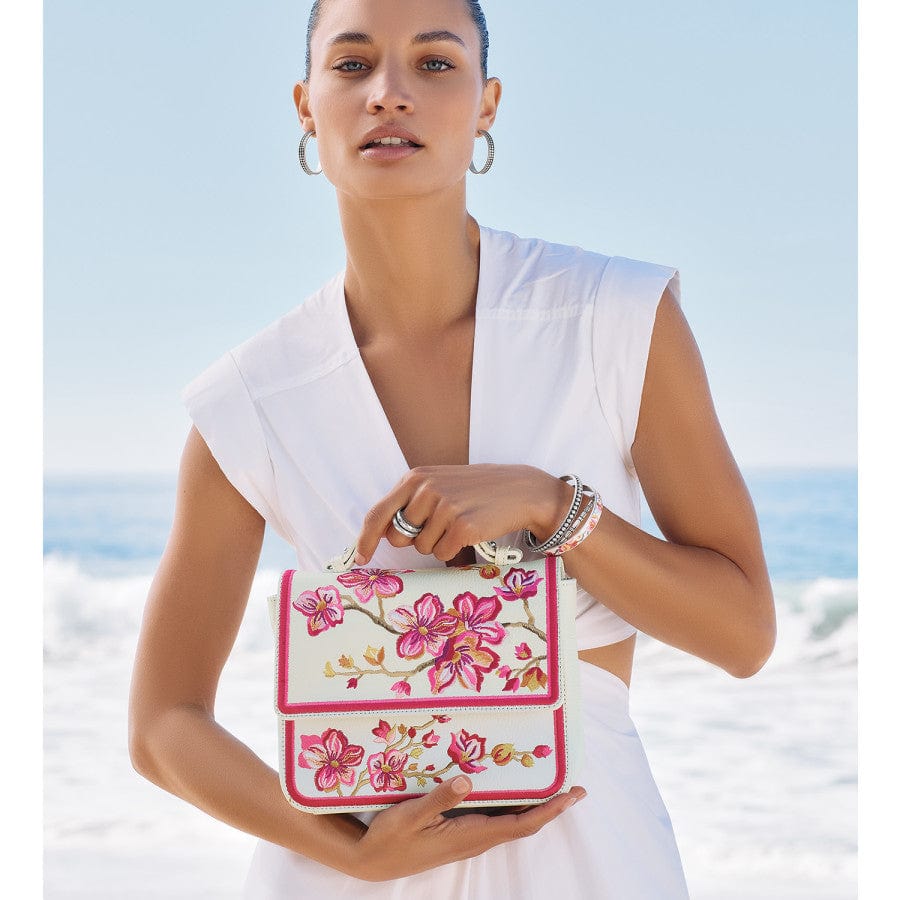 Model holding Kyoto In Bloom Miya Flap Bag on a beach with matching white outfit