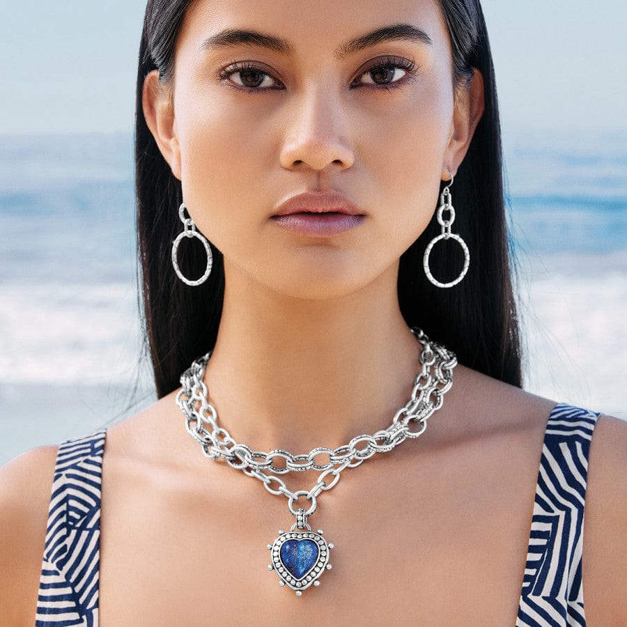 Model wearing Pebble Dot Hati Lapis Heart Necklace with hoop earrings on standing on beach