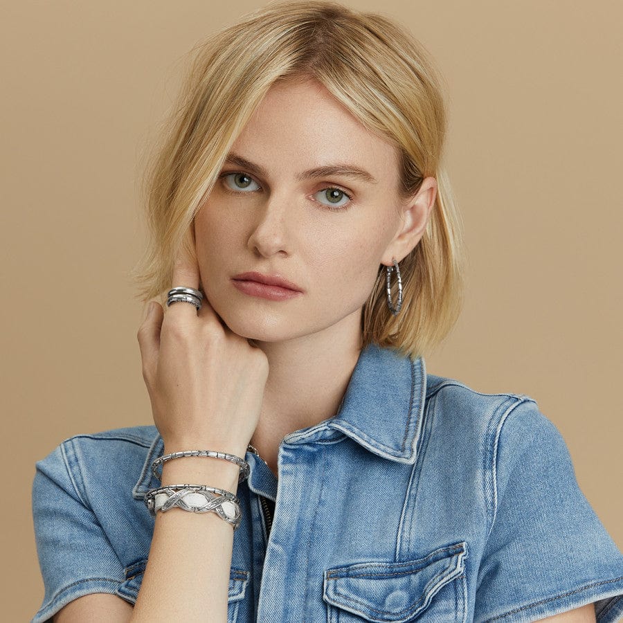 A model wearing Pebble Large Hoop Earrings with hair covering one ear with multiple matching silver bracelets, against a tan background.