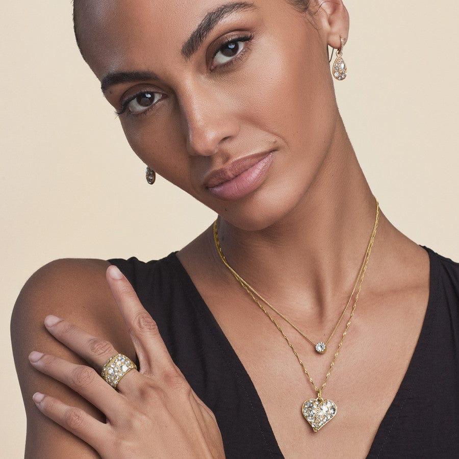 A woman wearing the Trust Your Journey Golden Heart Necklace, a heart-shaped pendant with matching earrings, and rings against a neutral background.