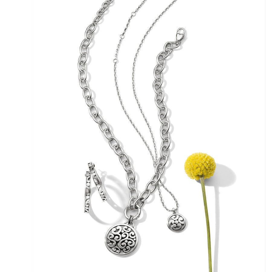 Brighton Contempo Medallion Charm Necklace featuring an intricately designed silver medallion pendant with scrollwork details, suspended from a polished silver chain, shown with a yellow flower